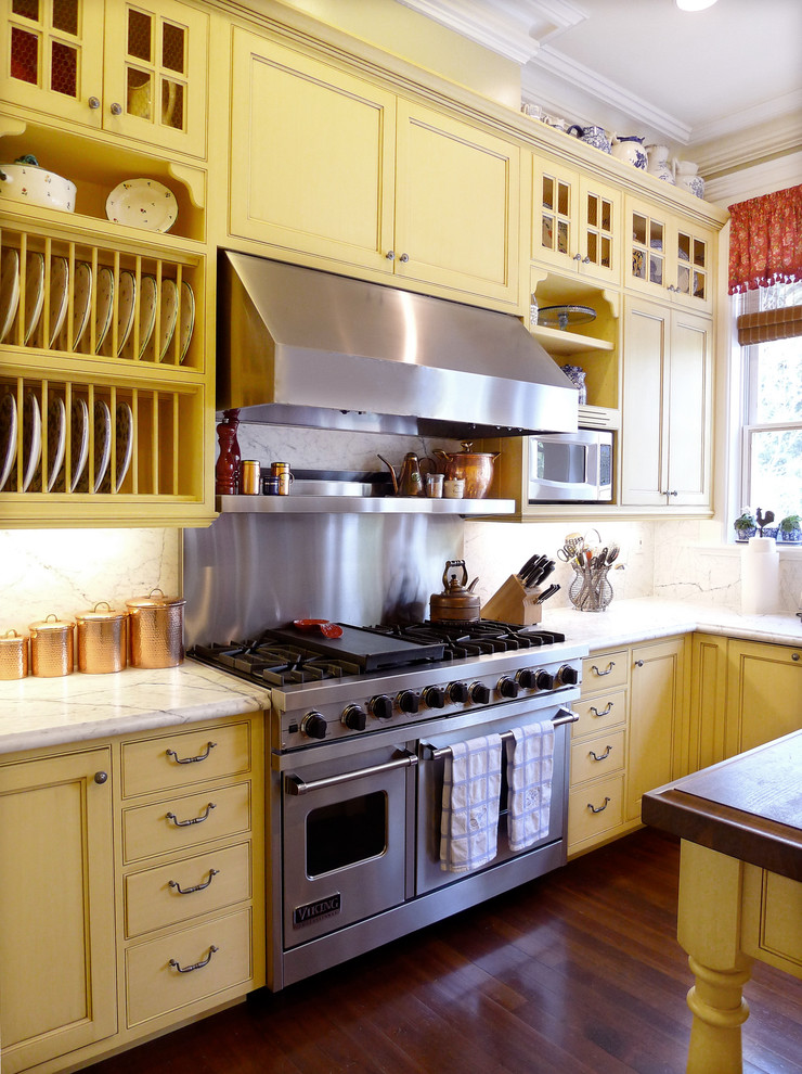 Immagine di una cucina classica con elettrodomestici in acciaio inossidabile, ante gialle, ante con riquadro incassato, paraspruzzi bianco e paraspruzzi in lastra di pietra