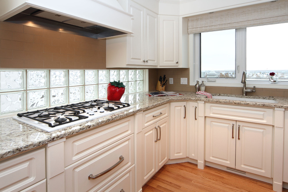 Bild på ett mellanstort vintage kök, med en undermonterad diskho, luckor med upphöjd panel, vita skåp, granitbänkskiva, glaspanel som stänkskydd, vita vitvaror, ljust trägolv och en köksö