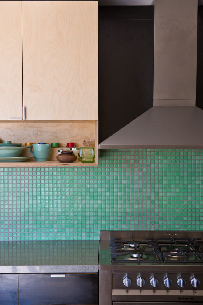 Bild på ett mellanstort funkis kök, med en undermonterad diskho, släta luckor, svarta skåp, bänkskiva i kvarts, grönt stänkskydd, stänkskydd i mosaik, rostfria vitvaror, ljust trägolv och en köksö