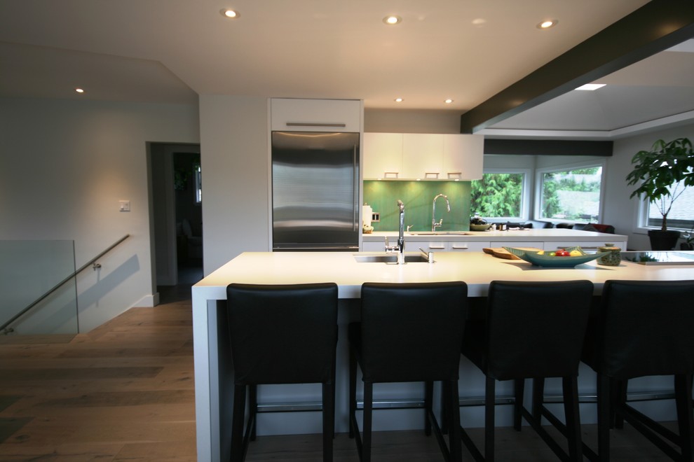 Foto på ett stort funkis kök, med en undermonterad diskho, släta luckor, grå skåp, bänkskiva i kvartsit, grönt stänkskydd, stänkskydd i cementkakel, rostfria vitvaror, mellanmörkt trägolv och en köksö