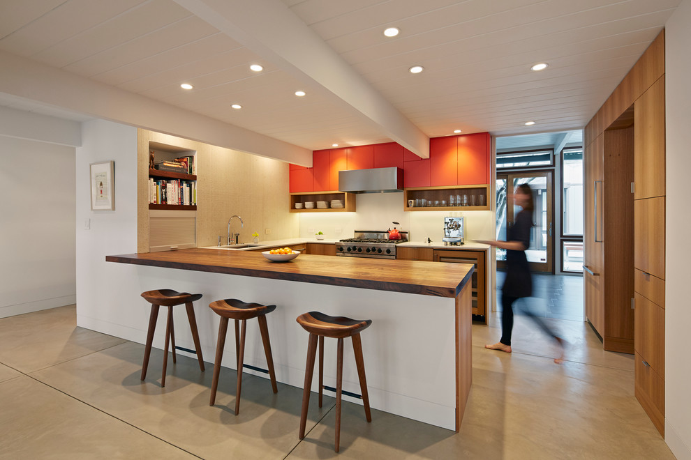 Foto på ett retro u-kök, med släta luckor, orange skåp, träbänkskiva, rostfria vitvaror och betonggolv
