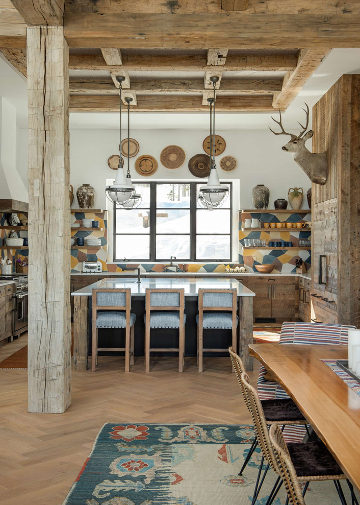 Aménagement d'une cuisine américaine montagne en U et bois vieilli avec une crédence multicolore, parquet clair, îlot, un plan de travail blanc et un plafond à caissons.