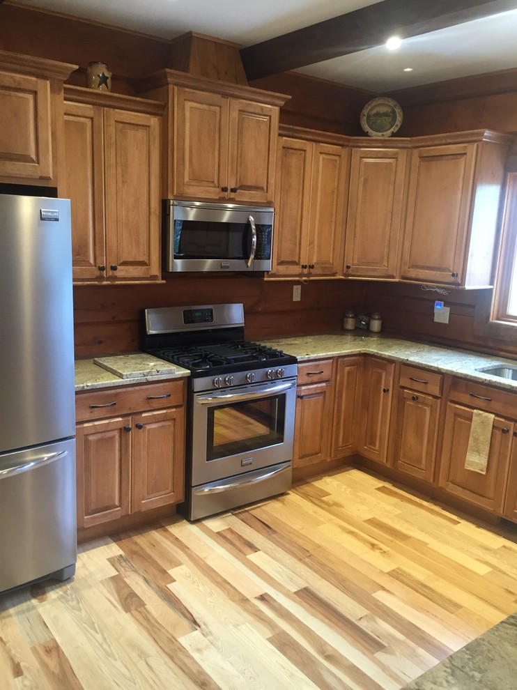 Example of a mid-sized mountain style u-shaped light wood floor and brown floor kitchen design in New York with an undermount sink, raised-panel cabinets, medium tone wood cabinets, granite countertops, wood backsplash, stainless steel appliances and no island