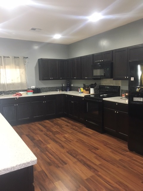 Large transitional u-shaped brown floor eat-in kitchen photo in Wichita with an integrated sink, recessed-panel cabinets, dark wood cabinets, solid surface countertops, black backsplash, glass tile backsplash, black appliances and a peninsula