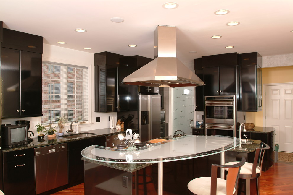 Bild på ett mellanstort funkis kök, med en undermonterad diskho, släta luckor, svarta skåp, granitbänkskiva, rostfria vitvaror, mellanmörkt trägolv, en köksö och brunt golv