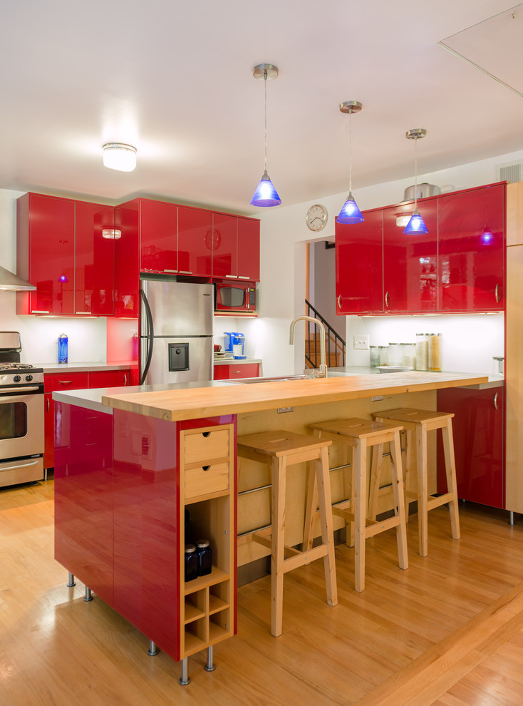 Modelo de cocina comedor lineal actual con fregadero encastrado, armarios con paneles lisos, puertas de armario rojas, encimera de madera, salpicadero blanco y electrodomésticos de acero inoxidable