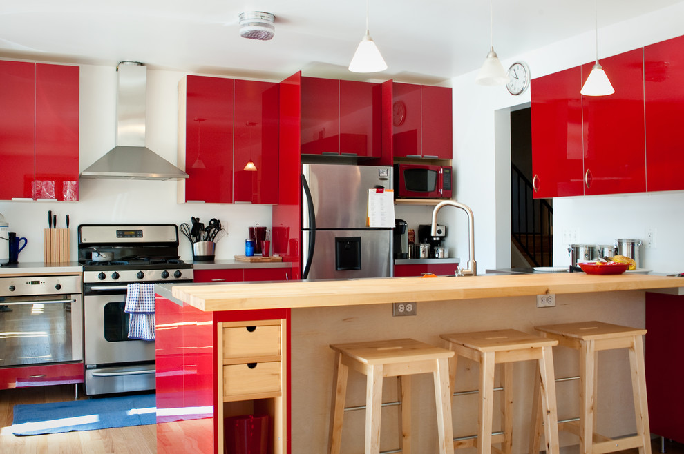 Imagen de cocina contemporánea con electrodomésticos de acero inoxidable, encimera de madera, puertas de armario rojas y armarios con paneles lisos