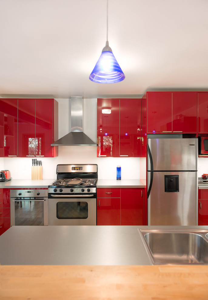 ワシントンD.C.にあるコンテンポラリースタイルのおしゃれなダイニングキッチン (フラットパネル扉のキャビネット、赤いキャビネット、ステンレスカウンター、シルバーの調理設備) の写真