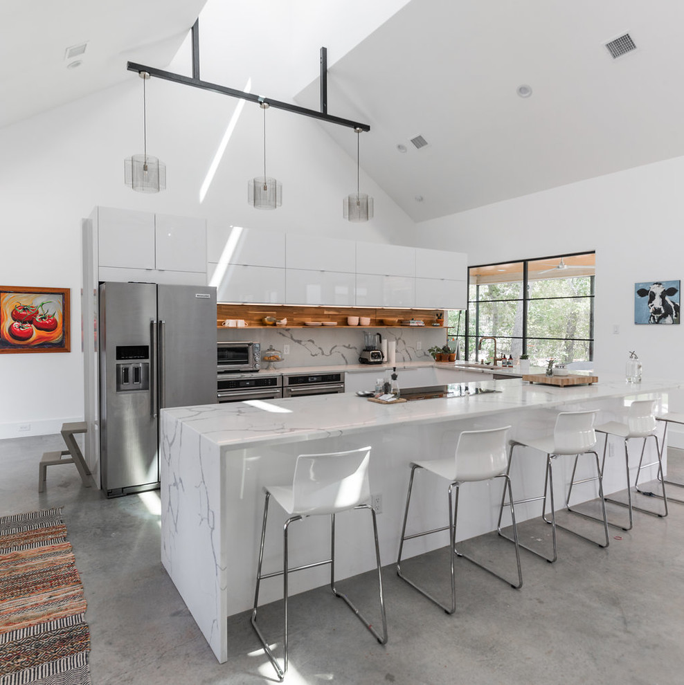 Example of a trendy u-shaped concrete floor and gray floor kitchen design in Austin with an undermount sink, flat-panel cabinets, white cabinets, white backsplash, stainless steel appliances, a peninsula and white countertops