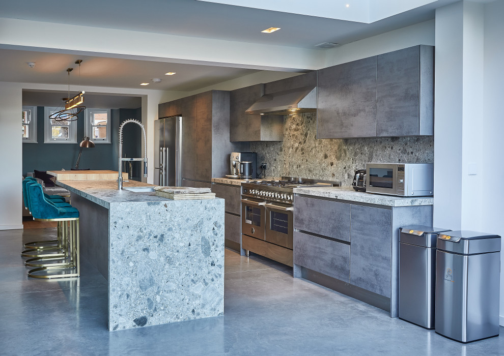 Trendy galley concrete floor and gray floor kitchen photo in London with flat-panel cabinets, gray cabinets, gray backsplash, stainless steel appliances, an island and gray countertops