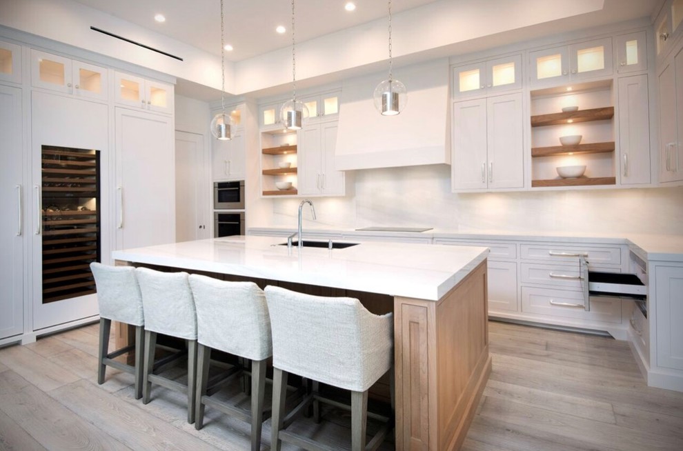 Large minimalist u-shaped light wood floor and beige floor eat-in kitchen photo with an undermount sink, shaker cabinets, white cabinets, white backsplash, paneled appliances, an island and white countertops