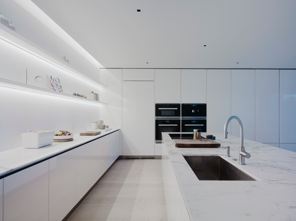 Inspiration för mellanstora moderna grått kök och matrum, med en enkel diskho, släta luckor, vita skåp, vitt stänkskydd, ljust trägolv, en köksö, marmorbänkskiva och vita vitvaror
