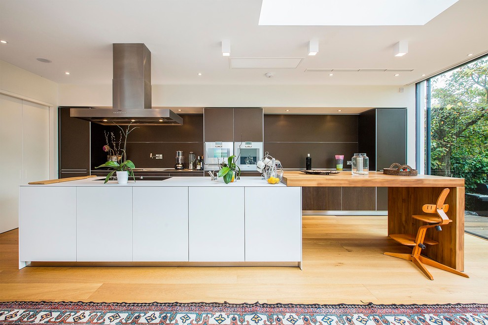 Zweizeilige Moderne Küchenbar mit flächenbündigen Schrankfronten, dunklen Holzschränken, Küchenrückwand in Braun, Elektrogeräten mit Frontblende, hellem Holzboden und Kücheninsel in London