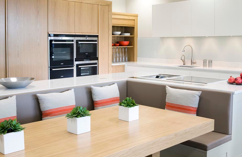 Photo of a large contemporary l-shaped kitchen/diner in London with white cabinets, composite countertops, white splashback, glass tiled splashback, stainless steel appliances, multiple islands and white worktops.