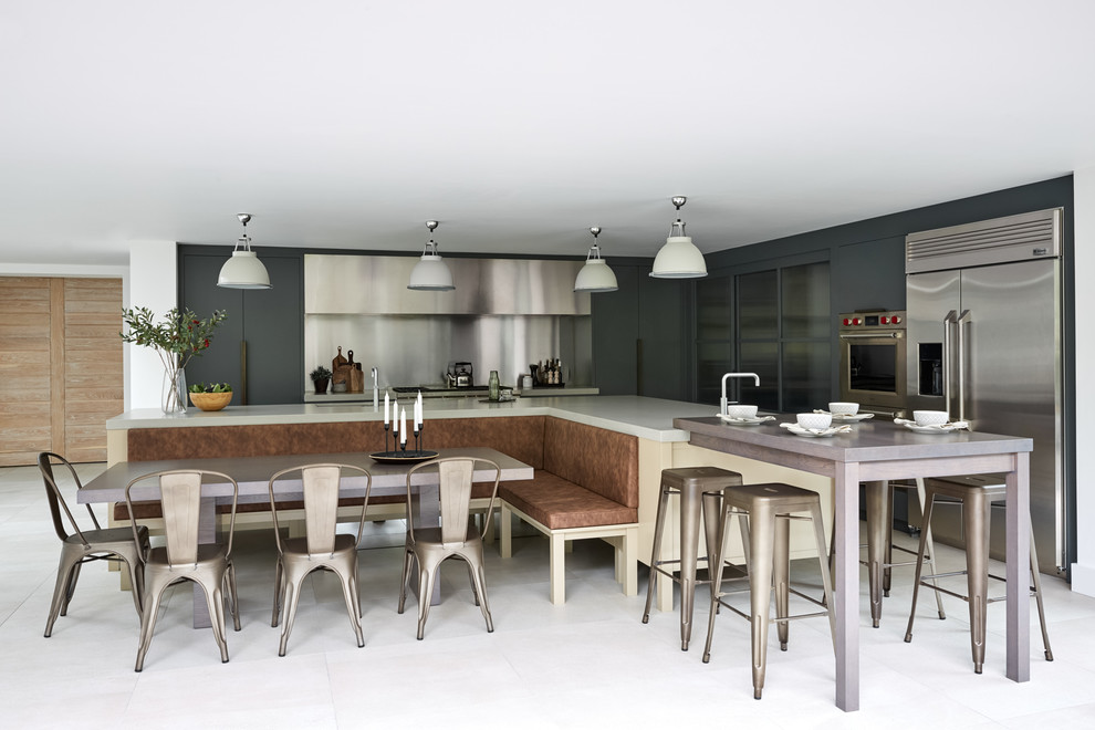 This is an example of a large contemporary l-shaped kitchen/diner in London with flat-panel cabinets, blue cabinets, composite countertops, metallic splashback, metal splashback, stainless steel appliances, multiple islands and white worktops.