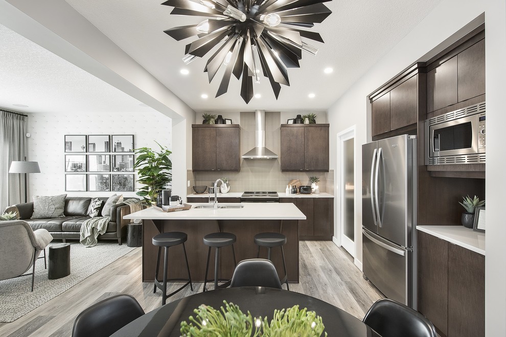 Example of a mid-sized trendy l-shaped eat-in kitchen design in Calgary with an undermount sink, flat-panel cabinets, dark wood cabinets, gray backsplash, stainless steel appliances, an island and white countertops
