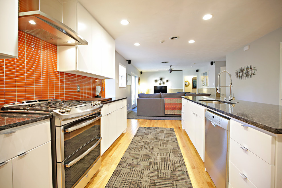 Moderne Wohnküche mit Einbauwaschbecken, flächenbündigen Schrankfronten, weißen Schränken, Granit-Arbeitsplatte, Küchenrückwand in Orange, Küchengeräten aus Edelstahl und hellem Holzboden in Dallas
