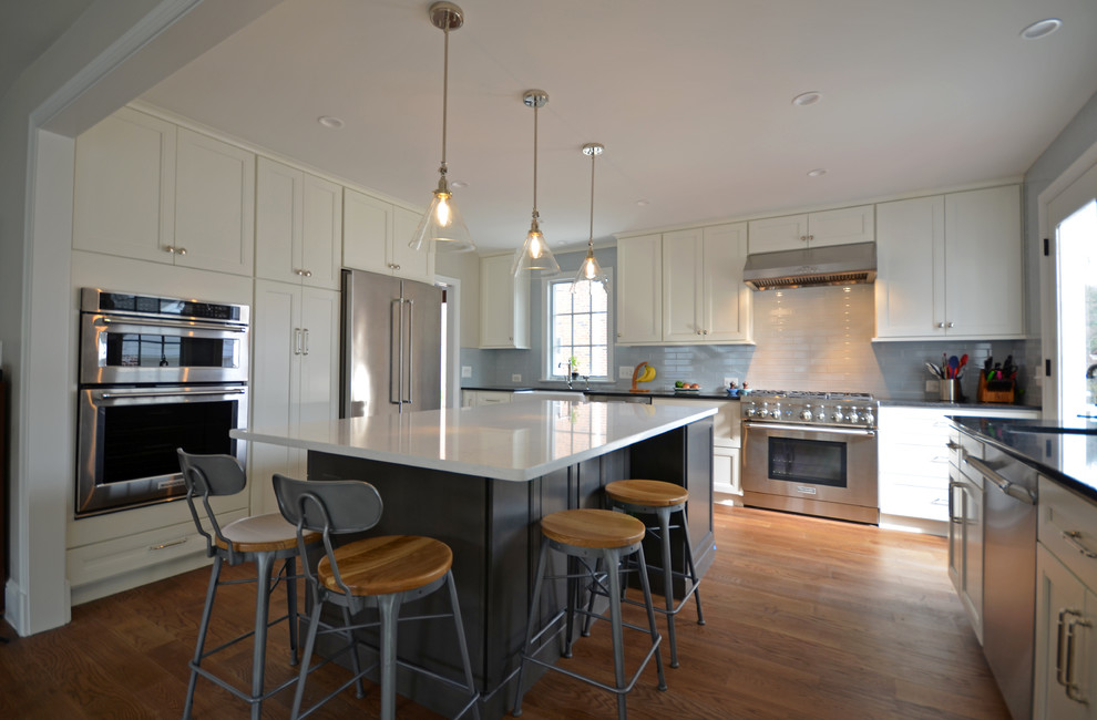 Eat-in kitchen - mid-sized traditional u-shaped medium tone wood floor and brown floor eat-in kitchen idea in DC Metro with a farmhouse sink, shaker cabinets, white cabinets, quartz countertops, blue backsplash, subway tile backsplash, stainless steel appliances, an island and white countertops
