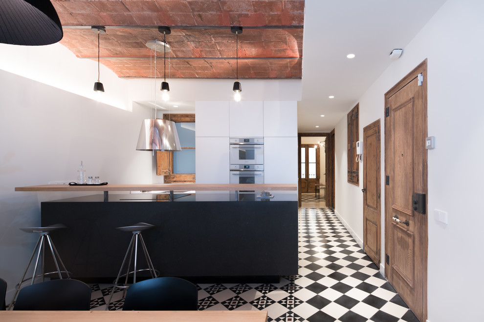 バルセロナにある地中海スタイルのおしゃれなキッチン (白いキャビネット、フラットパネル扉のキャビネット、シルバーの調理設備、マルチカラーの床、黒いキッチンカウンター) の写真