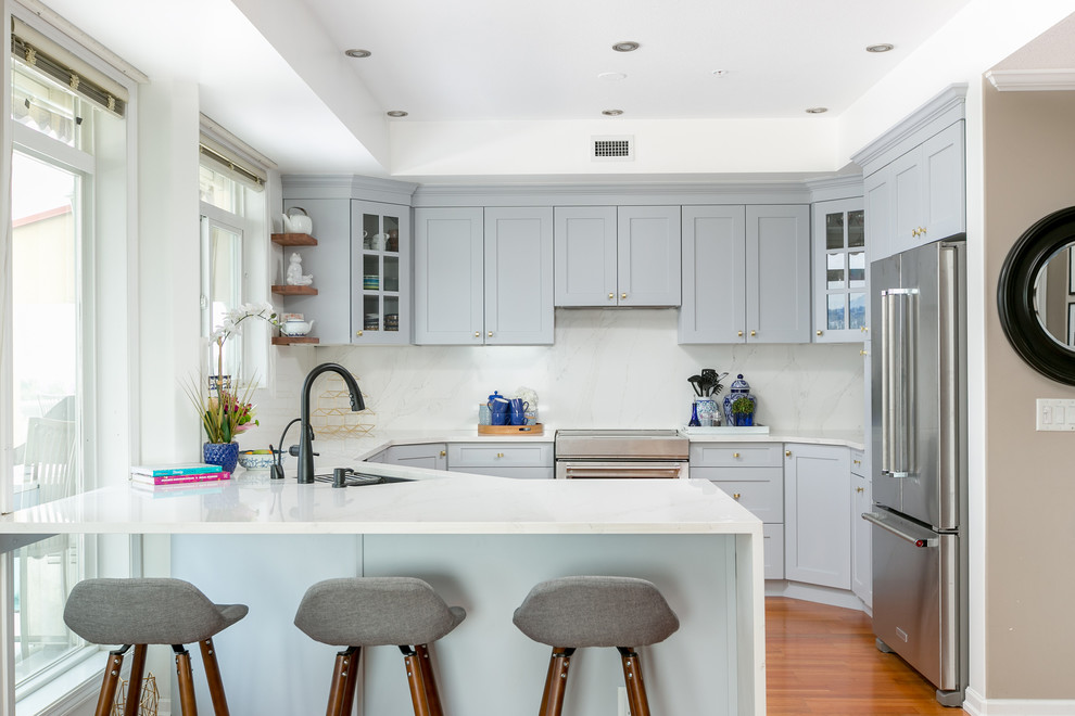 Inredning av ett modernt stort kök, med en undermonterad diskho, skåp i shakerstil, grå skåp, marmorbänkskiva, vitt stänkskydd, rostfria vitvaror, mellanmörkt trägolv, en halv köksö och brunt golv