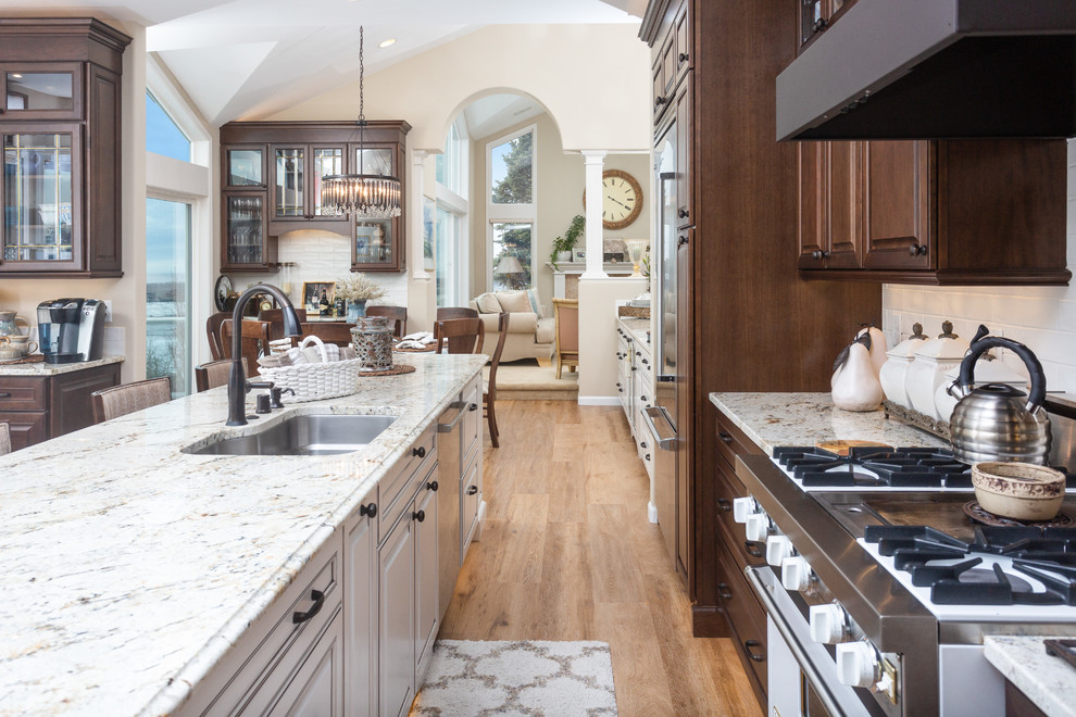 Inspiration for a huge timeless galley vinyl floor and beige floor eat-in kitchen remodel in Other with a single-bowl sink, raised-panel cabinets, dark wood cabinets, granite countertops, white backsplash, ceramic backsplash, stainless steel appliances, an island and beige countertops