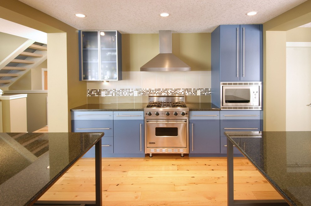 Einzeilige, Mittelgroße Moderne Wohnküche mit flächenbündigen Schrankfronten, blauen Schränken, Granit-Arbeitsplatte, bunter Rückwand, Rückwand aus Keramikfliesen, Küchengeräten aus Edelstahl, hellem Holzboden und zwei Kücheninseln in Calgary