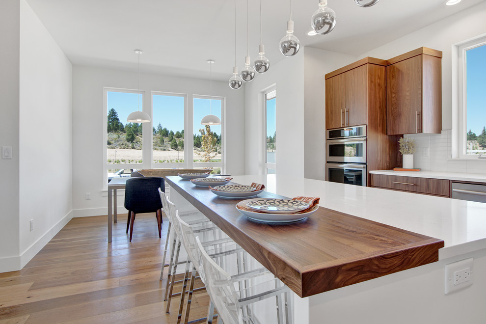 Example of a large trendy l-shaped light wood floor eat-in kitchen design in Portland with a drop-in sink, flat-panel cabinets, medium tone wood cabinets, quartz countertops, white backsplash, subway tile backsplash, stainless steel appliances and an island
