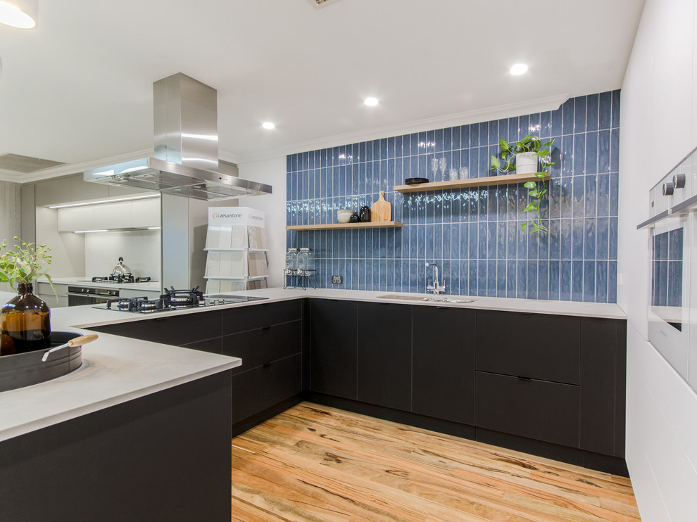 Inspiration for a medium sized industrial u-shaped enclosed kitchen in Perth with a double-bowl sink, flat-panel cabinets, black cabinets, engineered stone countertops, blue splashback, metro tiled splashback, white appliances, medium hardwood flooring, no island, brown floors and white worktops.