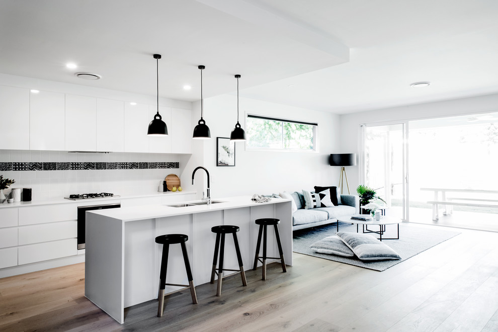 Open concept kitchen - scandinavian galley light wood floor and beige floor open concept kitchen idea in Brisbane with a double-bowl sink, flat-panel cabinets, white cabinets, white backsplash, black appliances and an island