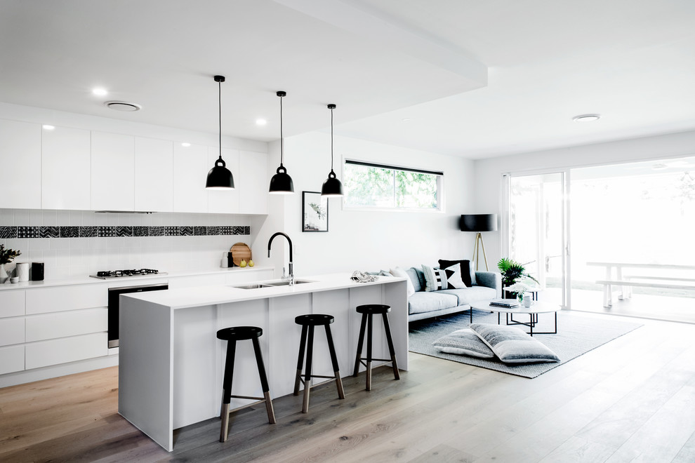 Пример оригинального дизайна: параллельная кухня-гостиная в скандинавском стиле с двойной мойкой, плоскими фасадами, белым фартуком, черной техникой, светлым паркетным полом, островом, бежевым полом и черно-белыми фасадами