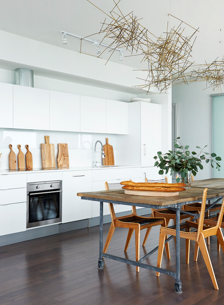 Photo of a small contemporary single-wall kitchen/diner in Toronto with flat-panel cabinets, white cabinets, composite countertops, glass sheet splashback, stainless steel appliances, white splashback, no island and medium hardwood flooring.