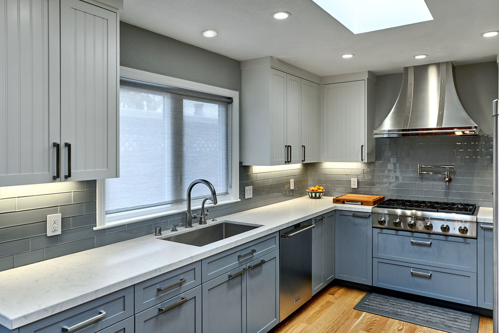 Inspiration for a mid-sized transitional u-shaped medium tone wood floor and brown floor open concept kitchen remodel in San Francisco with an undermount sink, louvered cabinets, blue cabinets, marble countertops, gray backsplash, glass tile backsplash, stainless steel appliances, no island and white countertops