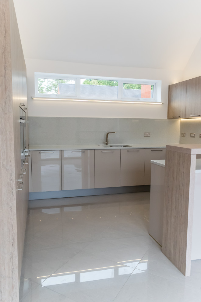 This is an example of a medium sized contemporary u-shaped open plan kitchen in Other with a submerged sink, flat-panel cabinets, beige cabinets, composite countertops, white splashback, glass sheet splashback, integrated appliances, ceramic flooring, a breakfast bar, white worktops, a vaulted ceiling and grey floors.