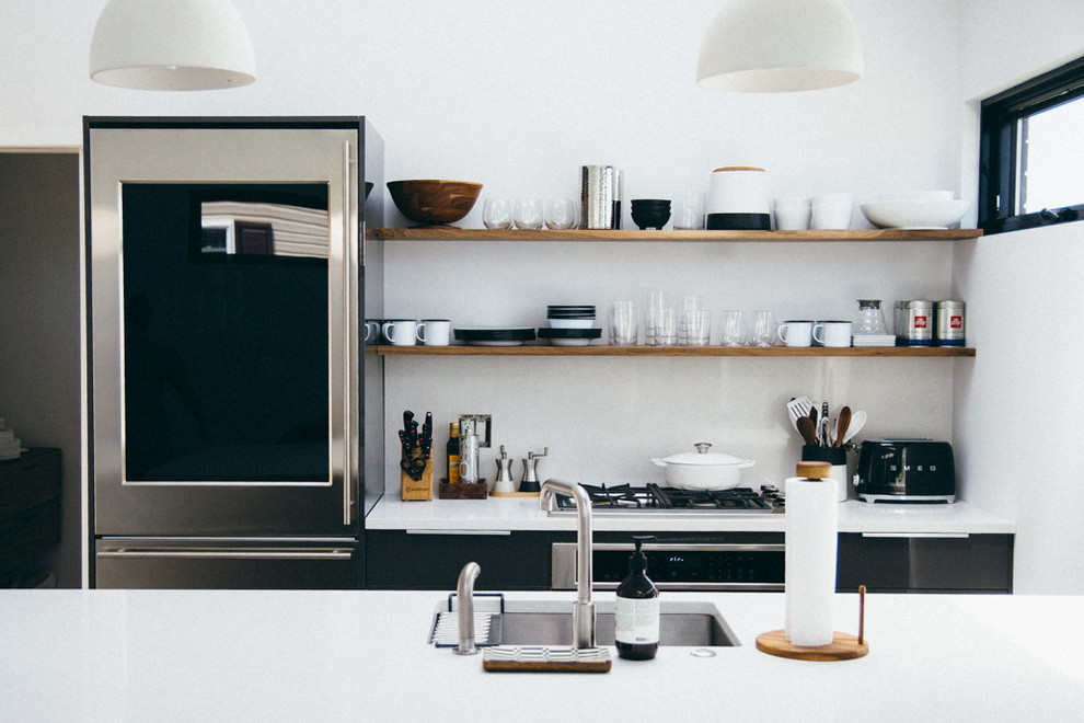 Exempel på ett litet modernt linjärt kök med öppen planlösning, med en undermonterad diskho, släta luckor, svarta skåp, bänkskiva i kvarts, vitt stänkskydd, rostfria vitvaror och en halv köksö