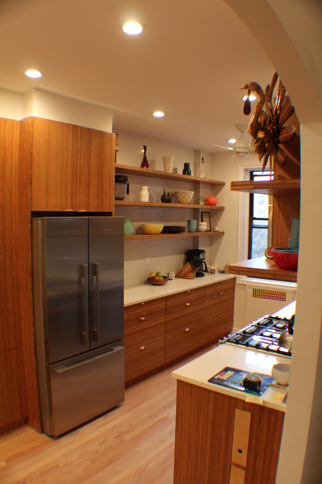 Idée de décoration pour une petite cuisine parallèle design en bois brun fermée avec un placard à porte plane, une crédence blanche, un électroménager en acier inoxydable, aucun îlot et parquet clair.