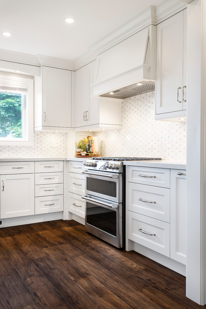 Inspiration for a large traditional u-shaped kitchen/diner in Toronto with a submerged sink, recessed-panel cabinets, white cabinets, engineered stone countertops, white splashback, ceramic splashback, stainless steel appliances, dark hardwood flooring, an island, brown floors and white worktops.