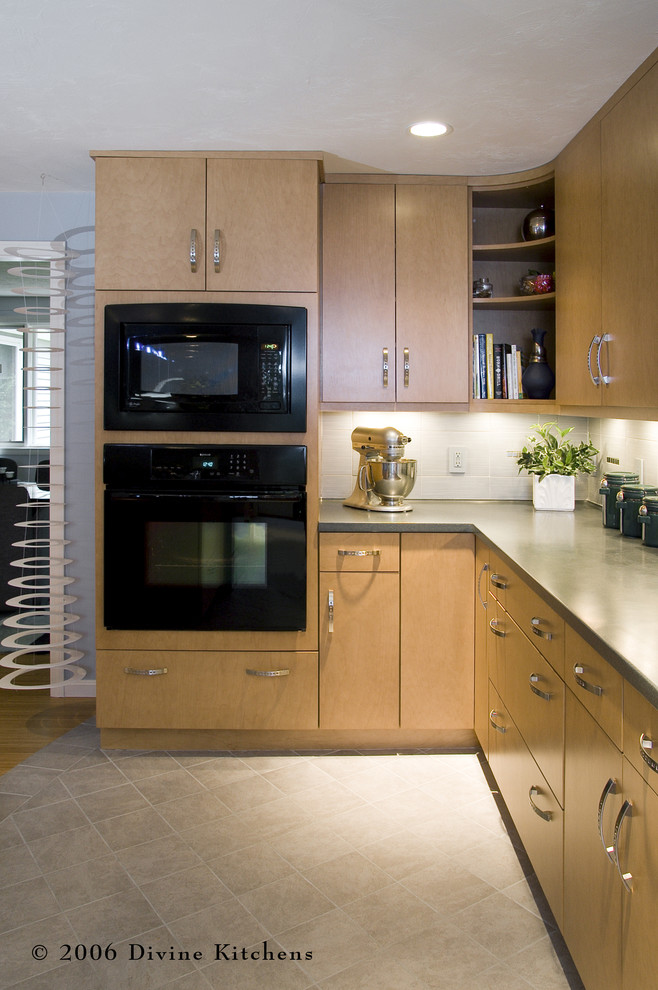 Photo of a large contemporary l-shaped kitchen/diner in Boston with a submerged sink, flat-panel cabinets, light wood cabinets, granite worktops, white splashback, ceramic splashback, black appliances, light hardwood flooring and an island.