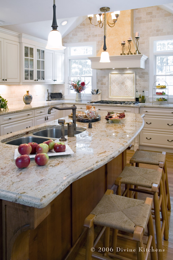 Inspiration for a large timeless l-shaped medium tone wood floor eat-in kitchen remodel in Boston with a double-bowl sink, raised-panel cabinets, white cabinets, granite countertops, beige backsplash, stone tile backsplash, stainless steel appliances and an island