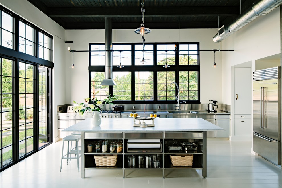 Bild på ett industriellt kök, med en integrerad diskho, skåp i rostfritt stål, stänkskydd med metallisk yta, stänkskydd i metallkakel, rostfria vitvaror, marmorbänkskiva och släta luckor
