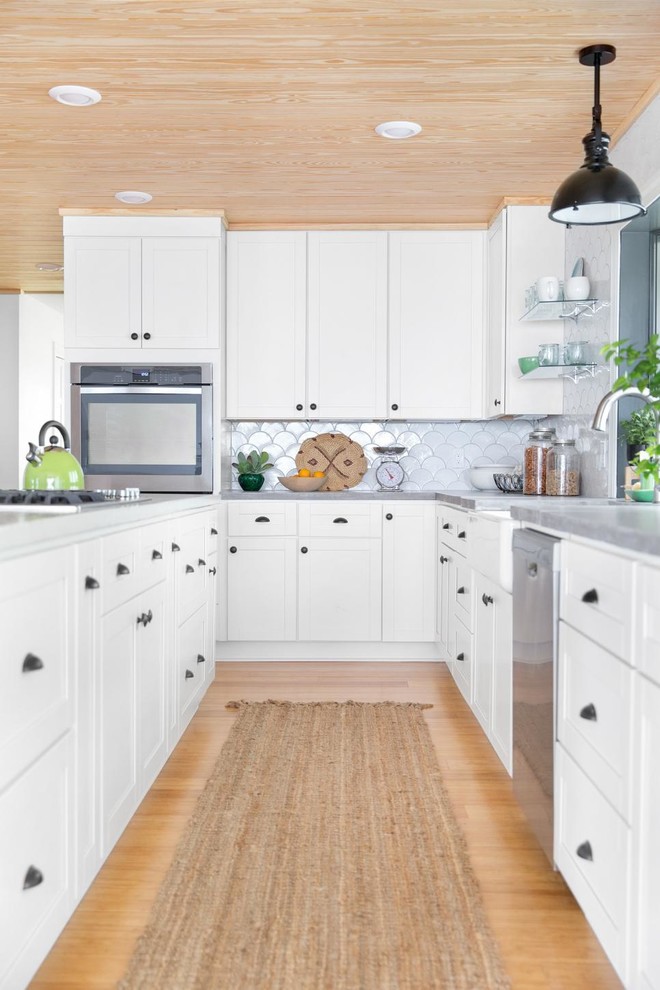 Design ideas for a traditional l-shaped kitchen in Orlando with a belfast sink, shaker cabinets, white splashback, ceramic splashback, stainless steel appliances, bamboo flooring, white cabinets, an island and concrete worktops.