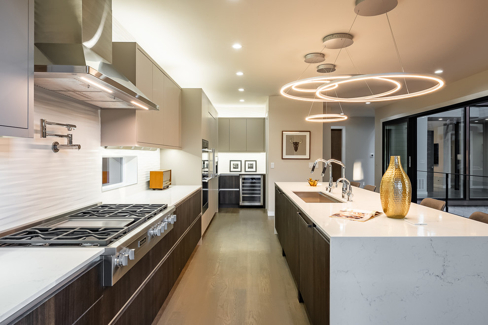 This is an example of a contemporary l-shaped kitchen/diner in Seattle with a submerged sink, quartz worktops, white splashback, porcelain splashback, stainless steel appliances, medium hardwood flooring, an island, brown floors and white worktops.