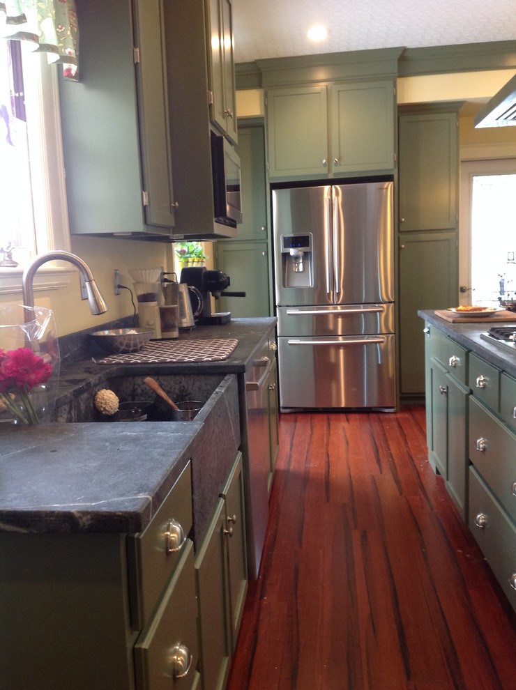 Klassische Küche mit Landhausspüle, Speckstein-Arbeitsplatte, Küchengeräten aus Edelstahl, grünen Schränken und braunem Holzboden in Sonstige