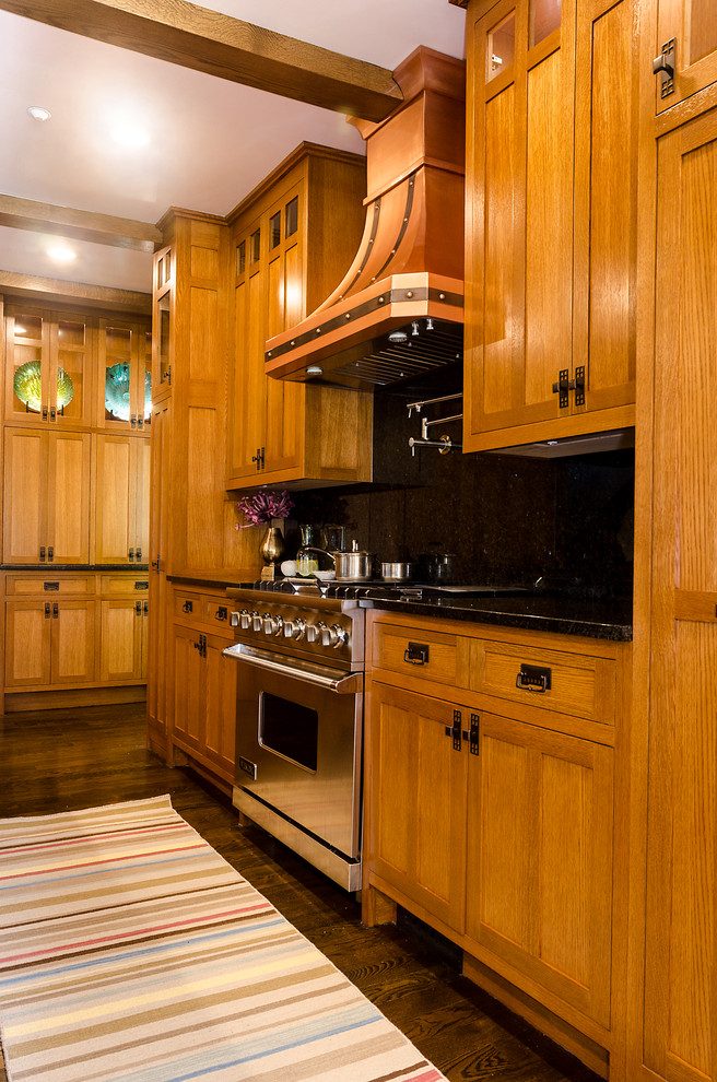 Foto på ett stort amerikanskt kök, med mörkt trägolv, en nedsänkt diskho, luckor med infälld panel, skåp i mellenmörkt trä, granitbänkskiva, svart stänkskydd, stänkskydd i sten, rostfria vitvaror och en köksö