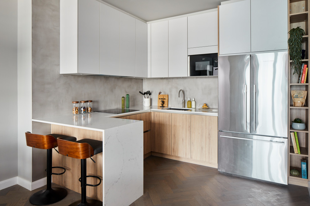 Inredning av ett modernt mellanstort vit vitt l-kök, med en undermonterad diskho, släta luckor, beige skåp, grått stänkskydd, stänkskydd i porslinskakel, rostfria vitvaror, en halv köksö och brunt golv