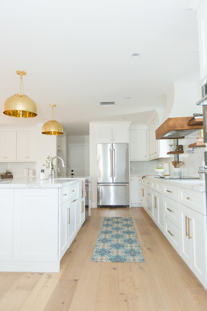 Exemple d'une cuisine chic en U avec un placard à porte shaker, des portes de placard blanches, une crédence blanche, un électroménager en acier inoxydable, parquet clair, un sol beige et un plan de travail blanc.