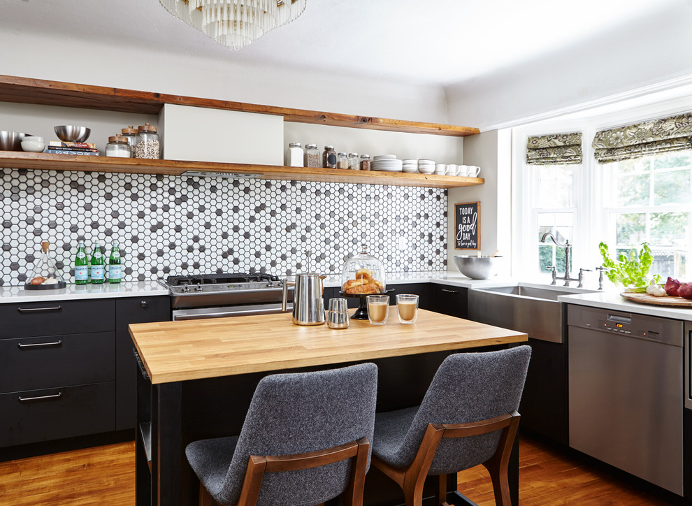 Inspiration for a traditional l-shaped kitchen in Toronto with a belfast sink, flat-panel cabinets, black splashback, mosaic tiled splashback, stainless steel appliances, medium hardwood flooring, an island and white worktops.