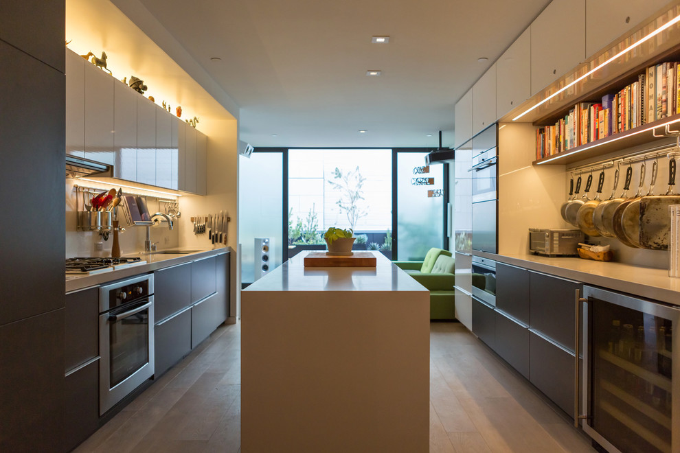 This is an example of a small modern galley open plan kitchen in San Francisco with a submerged sink, flat-panel cabinets, grey cabinets, engineered stone countertops, white splashback, stainless steel appliances, light hardwood flooring and an island.