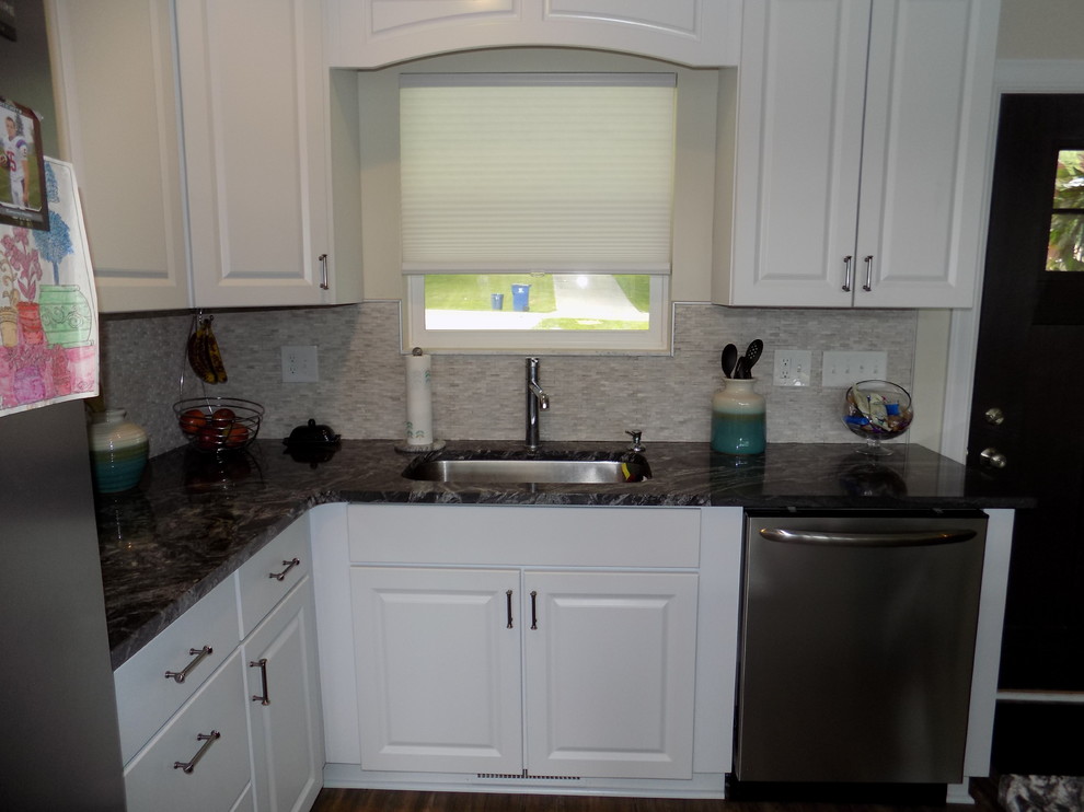 Bild på ett litet maritimt kök, med en undermonterad diskho, luckor med upphöjd panel, vita skåp, granitbänkskiva, beige stänkskydd, stänkskydd i stenkakel, rostfria vitvaror, mellanmörkt trägolv, en köksö och brunt golv