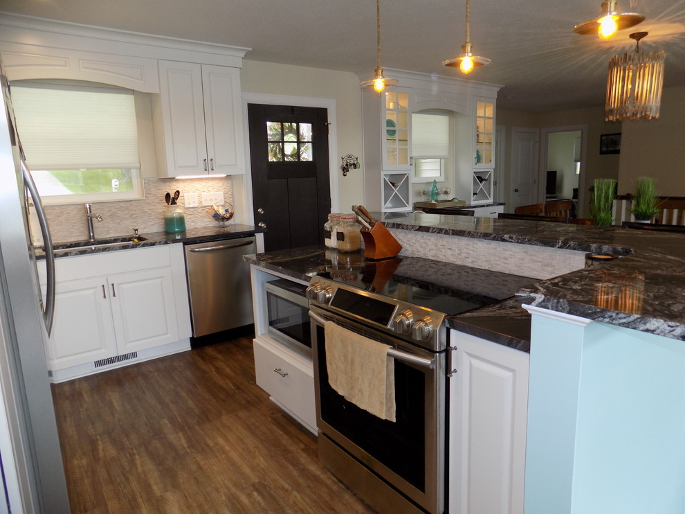 Foto på ett litet maritimt kök, med en undermonterad diskho, luckor med upphöjd panel, vita skåp, granitbänkskiva, beige stänkskydd, stänkskydd i stenkakel, rostfria vitvaror, mellanmörkt trägolv, en köksö och brunt golv
