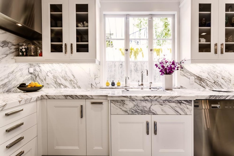 This is an example of an expansive bohemian u-shaped kitchen pantry in Los Angeles with a single-bowl sink, glass-front cabinets, white cabinets, marble worktops, stone slab splashback, stainless steel appliances, marble flooring and an island.